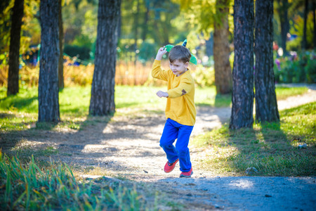 Happy kid playing with toy airplane against blue summer sky background. Boy throw foam plane in the forest or park. Best childhood concept.の写真素材