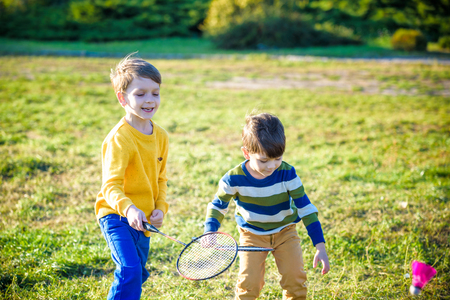 Two active preschool boy playing badminton in outdoor court in summer. Kids play tennis. School sports for children. Racquet and shuttlecock sport for child athlete. Friends happy together warm field.の写真素材