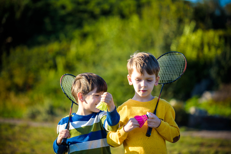 Two active preschool boy playing badminton in outdoor court in summer. Kids play tennis. School sports for children. Racquet and shuttlecock sport for child athlete. Friends happy together warm field.の写真素材