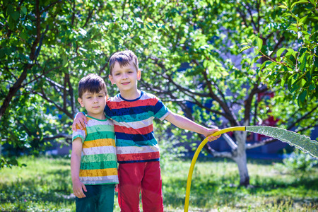 Child playing with garden sprinkler. Preschooler kid run and jump. Summer outdoor water fun in the backyard. Children play with hose watering flowers. Kids splash on sunny day. Selective focus on boy.の写真素材