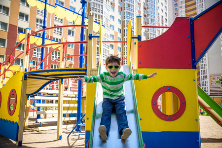 summer, childhood, leisure, friendship and people concept - happy little boy on children playground slid from the hill. Kid has a lot of fun.の写真素材