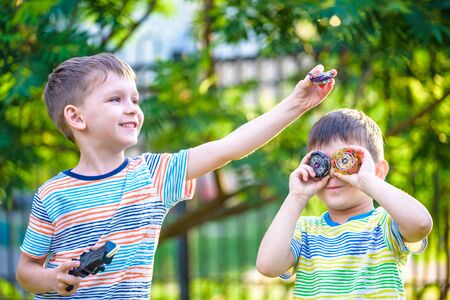 Two Boys playing with modern spin top outdoors. Entertainment game for children. Top, triggered by a trigger. Kids having a tournament on arena or battle field.の写真素材