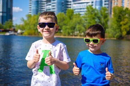 Portrait of happy kids on a bright sunny day on a bank of city river or lake. Friendship. Summer...