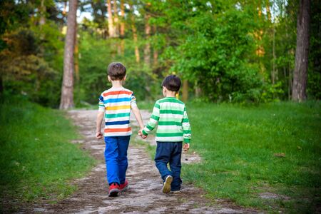 childhood, hiking, family, friendship and people concept - two happy kids walking along forest path.の写真素材