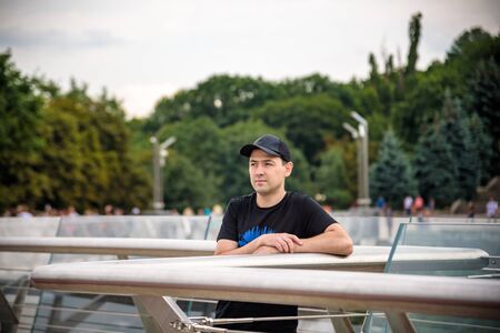 Hipster handsome male model with heat wearing black t-shirt. Standing on modern urban city view on...
