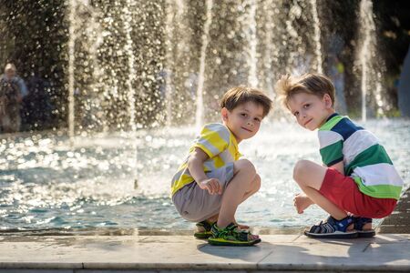 Cute toddler boy and older brothers, playing on a jet fountains with water splashing around,...