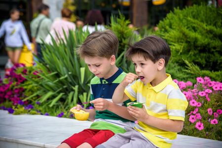 Tasty summer obsession concept. Happy young handsome hipster boys wearing colorful polo t-shirts, hugging, eating mini melts ice cream in heat cap over summer city park green nature plants background.の写真素材