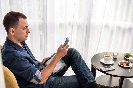 Portrait of male financial manager sitting at table with smartphone and tablet devices for making...