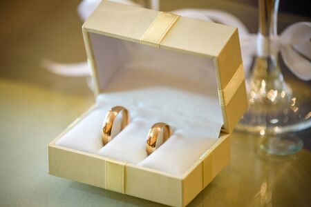 Two golden wedding rings in wooden box and branch of white acacia with flowers and leaves on wooden surface. Wedding card, Valentine's Day greeting. Wedding rings, copy space. Top view, flat lay.の写真素材