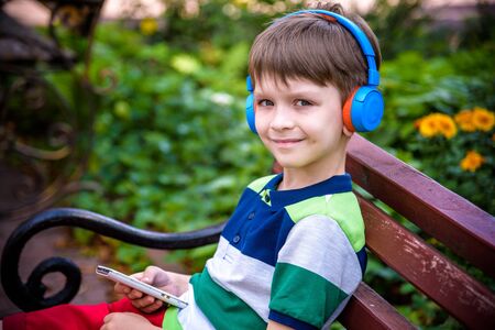 Boy listening music in headphones sitting on the bench and stares at the phone. after school. music relax concept.の写真素材