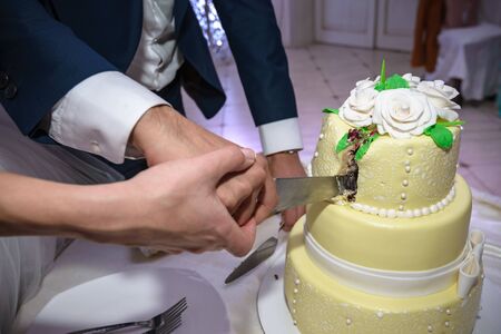 A wonderful wedding cake with the bride and groom cutting the cake with a long knife. The flowers look real, but are really edible sugar flowers.の写真素材