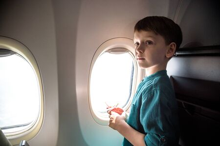 cute little boy traveling by an airplane. Child sitting by aircraft window and playing with toy plane. Traveling abroad with kids.の写真素材
