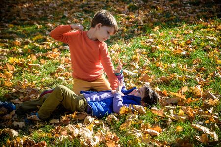 Two boys fighting outdoors. Friends wrestling in summer park. Siblings rivalry. Aggressive kid hold younger boy on ground, try to hit him.の写真素材