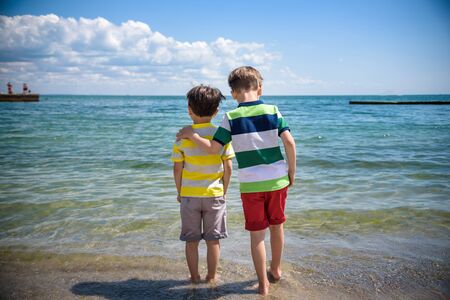 Two adorable little kid boys standing on lonely ocean beach. Child playing and looking on horizon. View from back. Preschool children sibling brother best friends enjoying summer vacations on sea.の写真素材