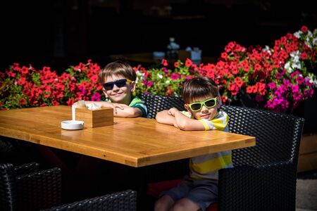 Two little kid boys waiting on table for healthy breakfast in hotel restaurant or city cafe. Summer holiday with children concept.の写真素材