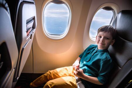cute little boy traveling by an airplane. Child sitting by aircraft window and playing with toy plane. Traveling abroad with kids.の写真素材