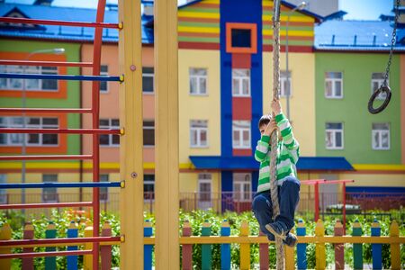 Cute little kid boy enjoying climbing rope on a playground. Toddler child learning to climb, having fun on warm sunny spring day. Active leisure with kidsの写真素材