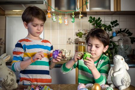 Two little kid boy coloring eggs for Easter holiday in domestic kitchen, indoors. Sibling brothers having fun and celebrating feast.の写真素材