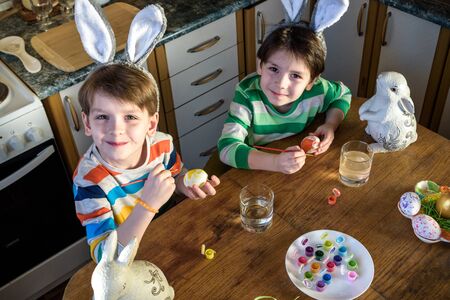 Two little kid boy coloring eggs for Easter holiday in domestic kitchen, indoors. Sibling brothers...