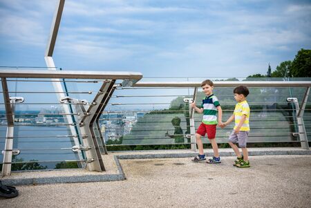 Portrait of two boys kid a walk over a bridge and looking down, child walking outside in sunny day, Young boys relaxing outdoors in summer on glass bridge. Tourism concept.の写真素材