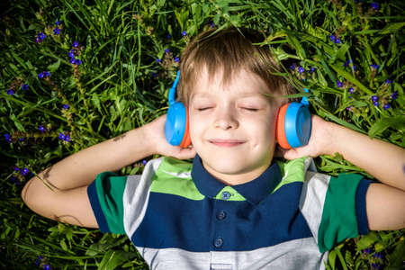 Smiling boy with arms under head lay under the sun on the green grass and listening music after school. Photo from above. Nature music relax concept.の写真素材