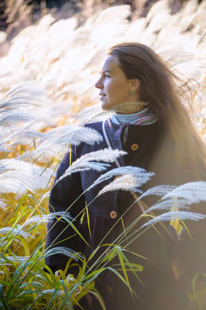 girl walks on nature among the reeds and shows her feelings and emotions. Romantic portrait of a young woman. Portrait of a beautiful Caucasian girl standing in yellow reed field in sunny autumn dayの写真素材