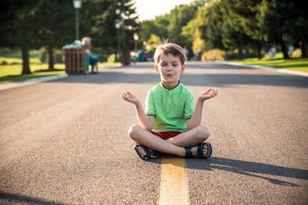 A boy is meditating sitting on the asphalt in the middle of the road. Spirit education relaxation concept.の写真素材