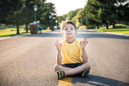 A boy is meditating sitting on the asphalt in the middle of the road. Spirit education relaxation concept.の写真素材