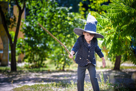 Toddler boy in pointed hat playing with magic wand outdoors. Little wizard. Halloween concept.の写真素材