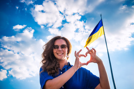 Young cheerful woman holding hands in form of heart on background of Ukrainian flag. Ukrainian patriot concept.の写真素材
