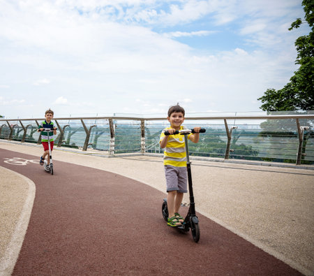 Two boy kids riding his scooter in the local park new glass bridge. Sunny summer day. Tourism concept.の写真素材