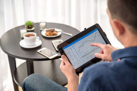 Man trading digital currencies online while relaxing by the cup of coffee in expencive hotel room.