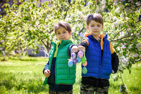 Two sibling brothers friends after successful egg hunt standing and smiling with Easter eggs in...