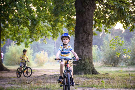 Two little kid boys in colorful casual clothes in summer forest park driving bicycle. Active children cycling on sunny fall day in nature. Safety, sports, leisure with kids concept.の写真素材