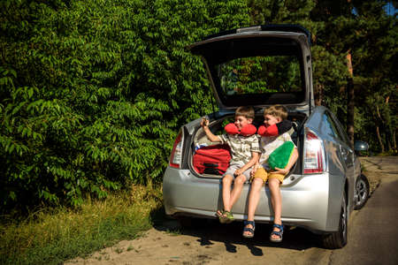 Two adorable little kids boy sitting in car trunk just before leaving for summer vacation. Sibling brothers making selfie on smartphone. Happy family going on long journey.の写真素材