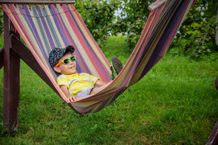 Cute little Caucasian boy relaxing and having fun in multicolored hammock in backyard or outdoor playground. Summer active leisure for kids. Child swinging on hammock. Activities for children.の写真素材
