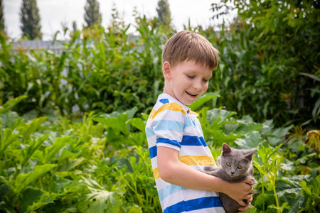 Funny boy hugging a cat with lots of love. Portrait of child holding on hands a Kitten. Playing with a cat on village countryside.の写真素材