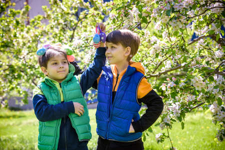 Two sibling brothers friends after successful egg hunt standing and smiling with Easter eggs in...