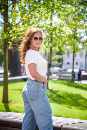 Close-up portrait of laughing brunette girl in casual clothes, sunglasses and jeans on city background. Lovable lady standing on city street and looking directly on camera.の写真素材