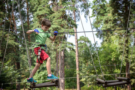 Strong excited young boy playing outdoors in rope park. Caucasian child dressed in casual clothes...