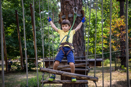 Strong excited young boy playing outdoors in rope park. Caucasian child dressed in casual clothes and sneakers at warm sunny day. Active leisure time with children concept.の写真素材