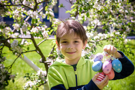 Different color Easter Eggs in a child's hands after egg hunt. Traditional Easter concept. Happy boy smiling on green blooming field background.の写真素材