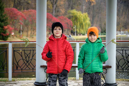 Two siblings stand on the bridge and admire the magnificent view of the autumn forest and its reflection in the lake water. Autumn walk. Outdoor lifestyle, active family lifestyle.の写真素材