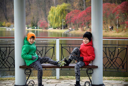 Two siblings stand on the bridge and admire the magnificent view of the autumn forest and its reflection in the lake water. Autumn walk. Outdoor lifestyle, active family lifestyle.の写真素材