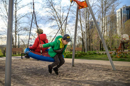 Two little kid boys having fun with swing on outdoor playground. Children, best friends and siblings...