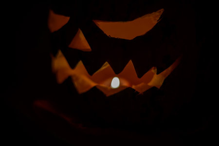 Halloween pumpkin smile and scary eyes for party night. Close up view of scary Halloween pumpkin with eyes glowing inside at black background. Selective focus.の写真素材