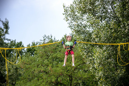 The boy is jumping on a bungee trampoline. A child with insurance and stretchable rubber bands hangs...