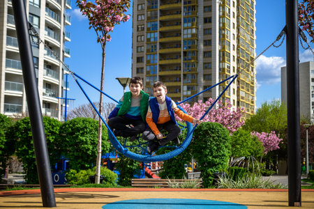 Cheerful boy with his toddler brother swinging in the swing-nest. Entertainment for preschoolers...