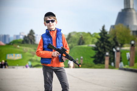 Boy make a picture on monument motherland and Ukrainian flag background. Kid hold in his arms toy...