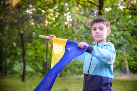 Ukrainian boy with waving flag and praying to stop the war in Ukraine in a field at sunset. War of...
